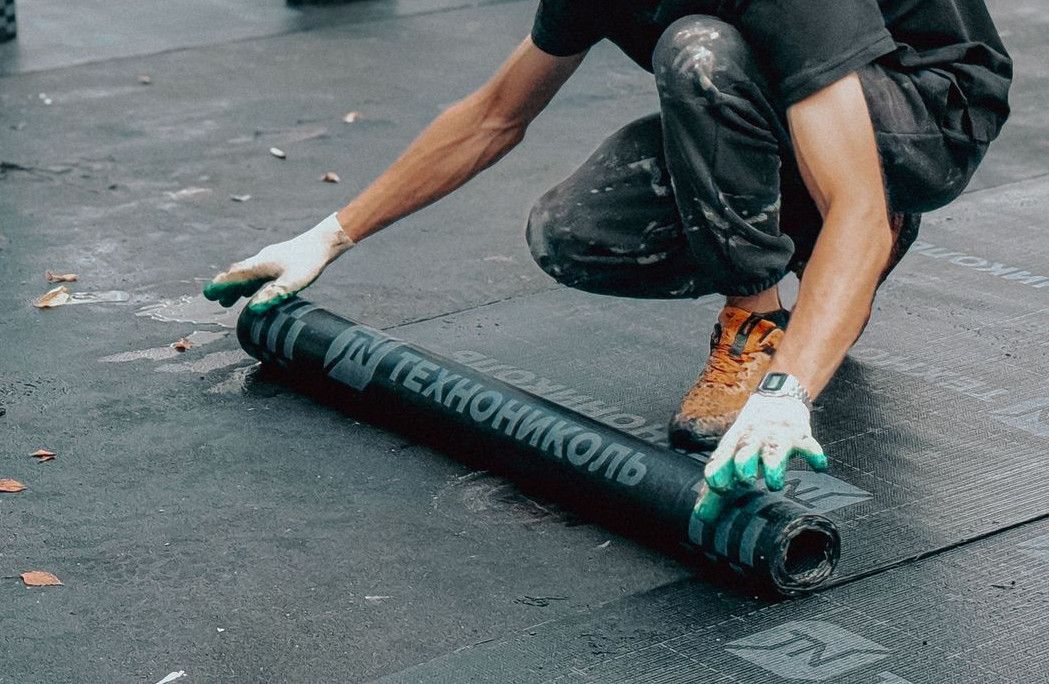 Construction worker applies waterproof membrane on rooftop for protection against weather elements.